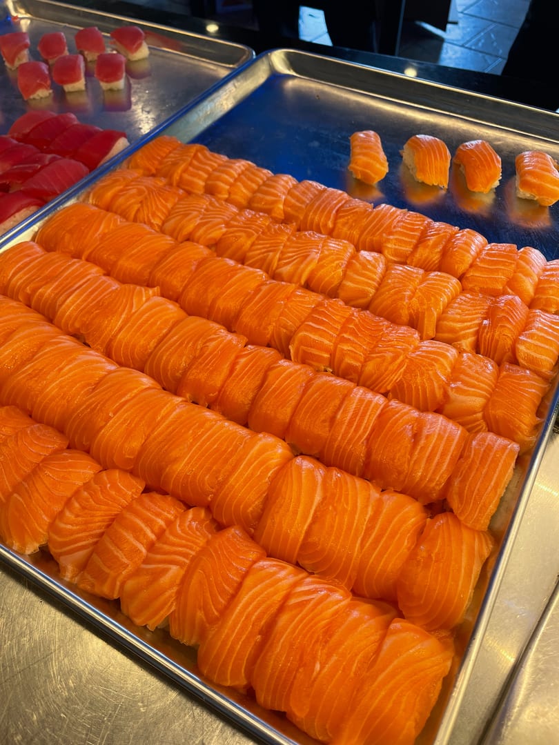 Rows of fresh salmon nigiri and tuna nigiri displayed on metal trays.