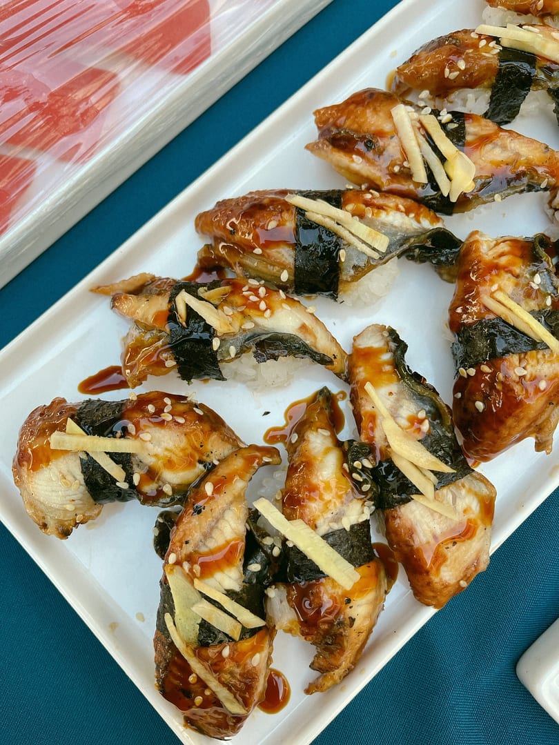 Unagi sushi with sweet sauce, sesame seeds, and ginger on a white rectangular plate.