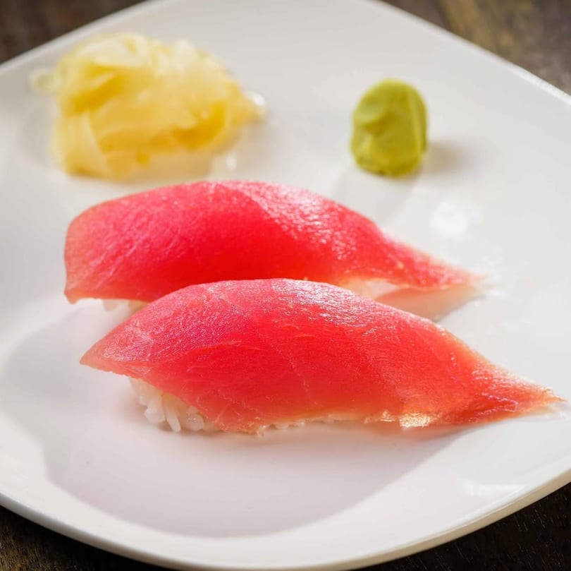 Two pieces of tuna nigiri sushi with pickled ginger and wasabi on a white plate.